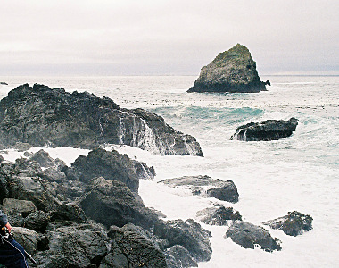 [There is a sea stack a few hundred yards out which is dry at the top, but the middle rocks and the ones closest to shore are getting parts lapped by waves.]